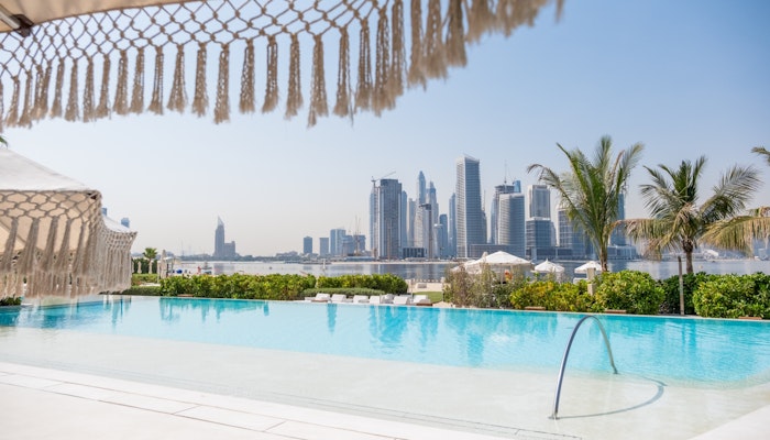 PLAYA Dubai A stylish pool area with lounge chairs and a view of the Dubai skyline.