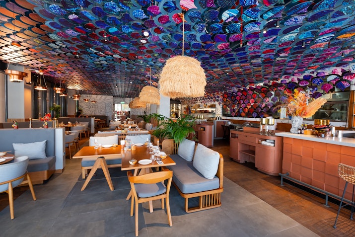 A modern restaurant interior featuring vibrant artwork on the ceiling, stylish seating arrangements, and an inviting atmosphere.