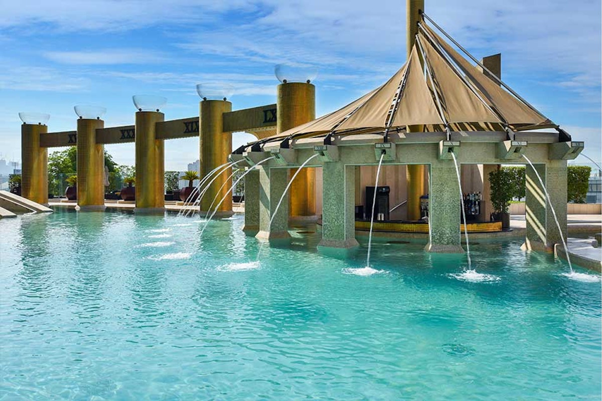 Raffles Dubai Resort-style pool with a thatched pavilion and water fountains, surrounded by tall columns and blue sky