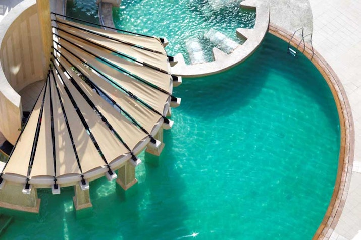 Aerial view of a circular pool with a spiral structure and shaded loungers
