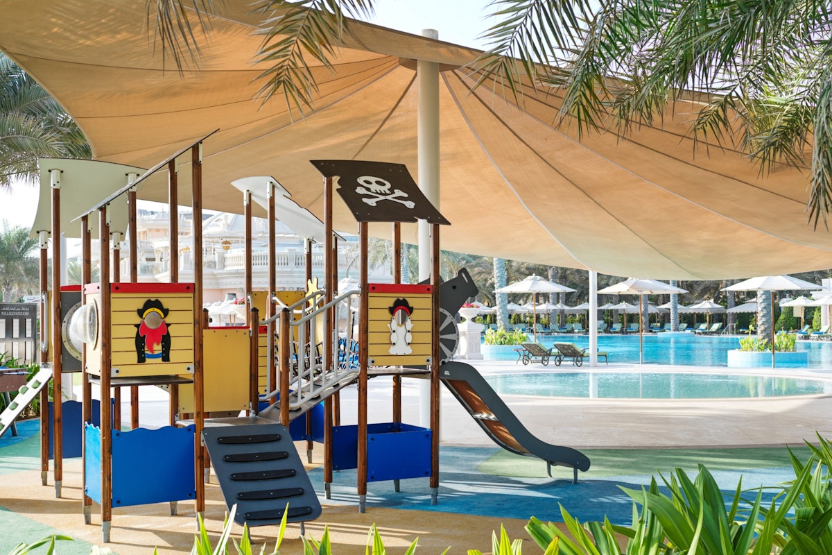 Raffles The Palm Dubai A pirate theme, complete with a slide and climbing structures, shaded by a large canopy, located near a swimming pool area.