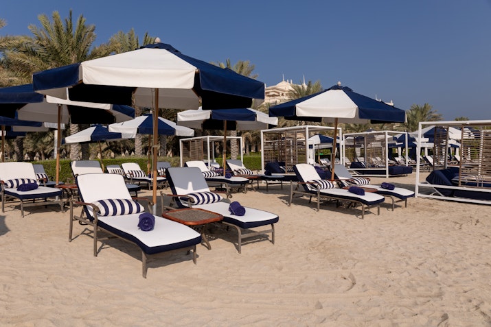 Lounge chairs with blue and white striped cushions and umbrellas, set on a sandy beach, providing a perfect relaxation spot under the sun.