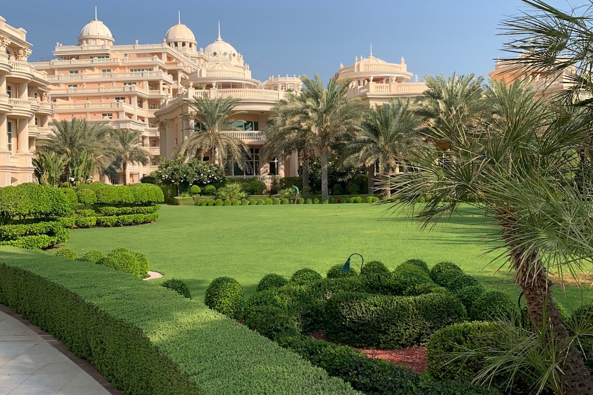 Raffles The Palm Dubai Garden with lush green lawns and neatly trimmed hedges, surrounded by an elegant hotel building characterized by domes and architectural detail.