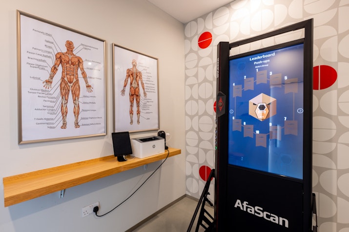 A room featuring an AfaScan machine next to anatomical charts of the human body on the wall and a wooden shelf with a computer.