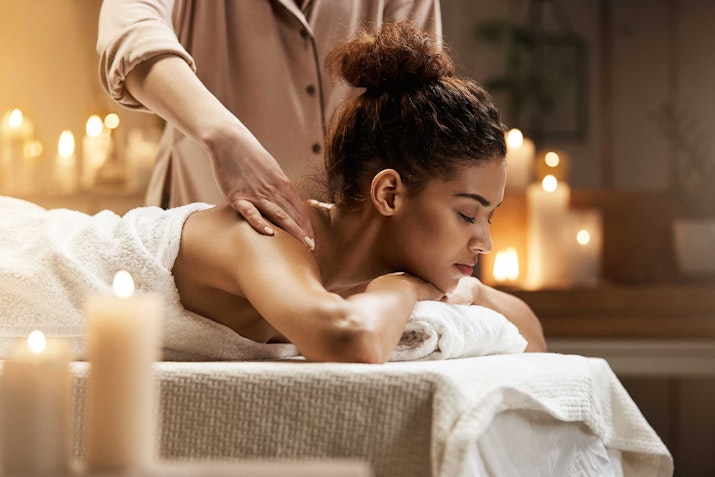 Shangri-La Dubai A woman receiving a massage in a serene spa environment, surrounded by candles.