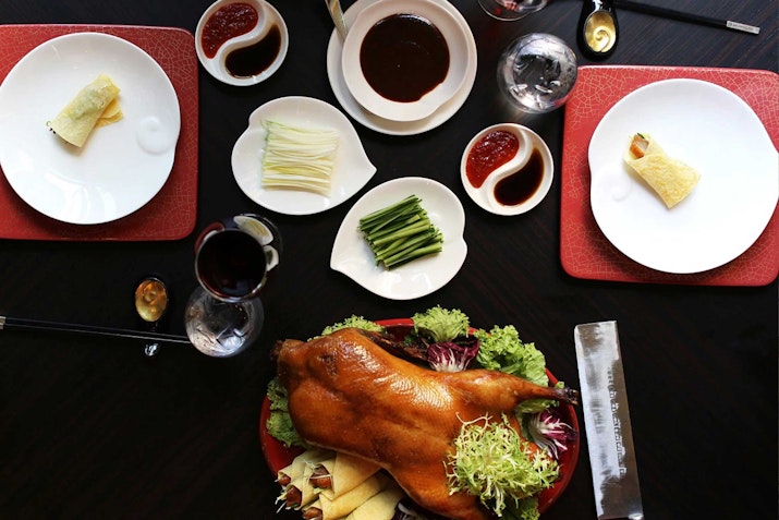 Shangri-La Qaryat al Beri A table set with a whole roasted duck surrounded by sauces, vegetables, and plates ready for serving.