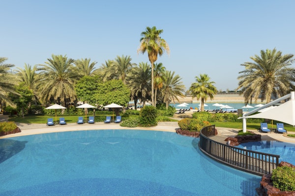 A tranquil resort pool area surrounded by lush greenery and palm trees, with sun loungers arranged neatly around the pool, creating an inviting atmosphere for relaxation.
