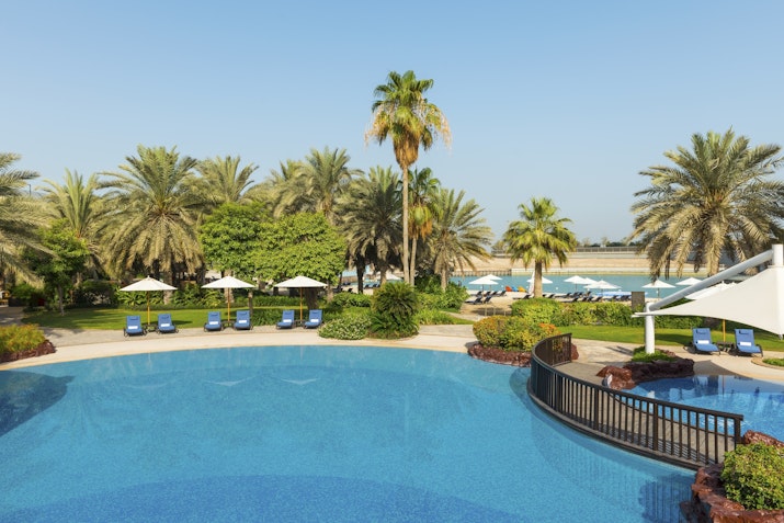 A tranquil resort pool area surrounded by lush greenery and palm trees, with sun loungers arranged neatly around the pool, creating an inviting atmosphere for relaxation.