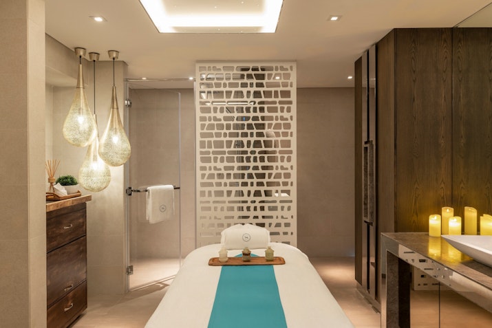 A serene spa treatment room featuring a massage table with a turquoise cover, ambient lighting, and decorative candles, creating a calming atmosphere.