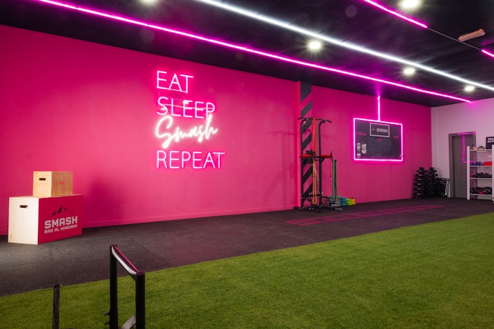 Bright fitness studio featuring a pink wall, neon sign, and sled track at SMASH Ras Al Khaimah's modern studio.