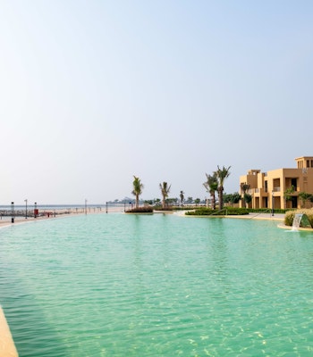 Sofitel Al Hamra Beach Resort A serene view of a waterway lined with palm trees and beachfront properties under a clear sky.