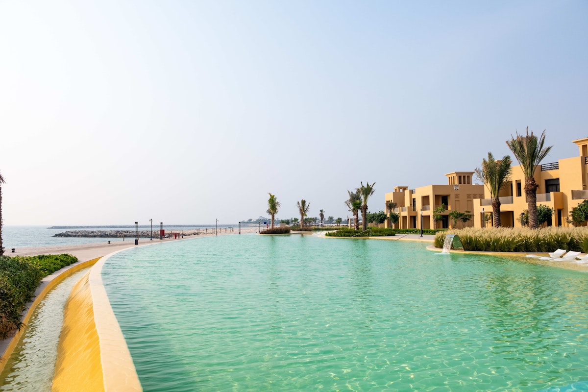 Sofitel Al Hamra Beach Resort A serene view of a waterway lined with palm trees and beachfront properties under a clear sky.