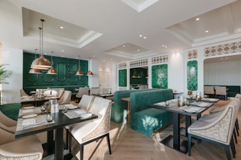 An elegant restaurant interior featuring stylish seating arrangements, green accents, and modern light fixtures, creating a sophisticated dining atmosphere.