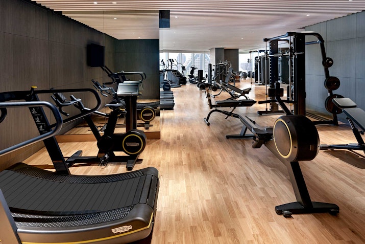 Modern gym with various exercise equipment and wood flooring.