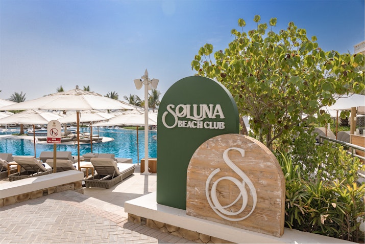 Club with a pool and sun loungers in the background under a clear blue sky.