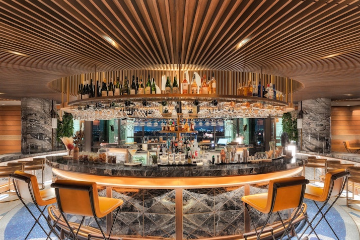 A modern bar with a circular design featuring a variety of bottles displayed on shelves, stylish bar stools, and elegant wooden accents.