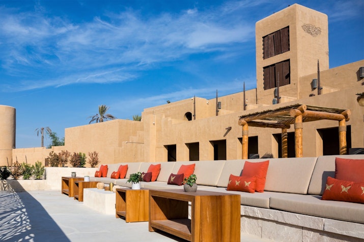 Comfortable outdoor seating with cushions, surrounded by traditional desert-style architecture under a bright blue sky.