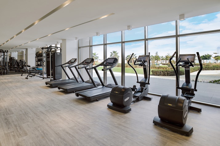 Gym with treadmills and exercise machines facing large windows with outdoor views.