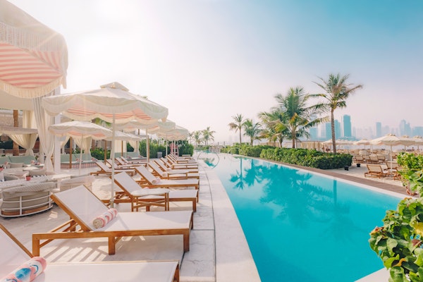 The 305 Dubai A serene poolside scene featuring lounge chairs with colorful towels, elegant cabanas, and palm trees, set against a backdrop of modern buildings and a clear sky.