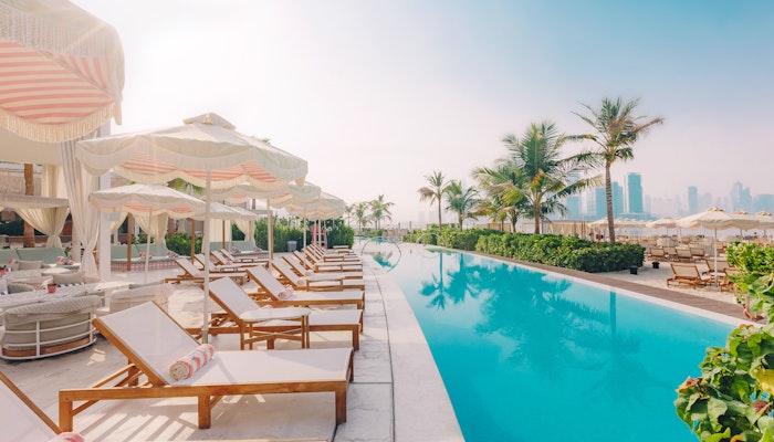 The 305 Dubai A serene poolside scene featuring lounge chairs with colorful towels, elegant cabanas, and palm trees, set against a backdrop of modern buildings and a clear sky.