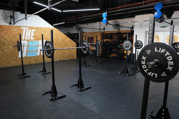 A spacious gym setup at The Den featuring squat racks and weightlifting equipment against a backdrop with The Den logo, designed for strength and conditioning training.