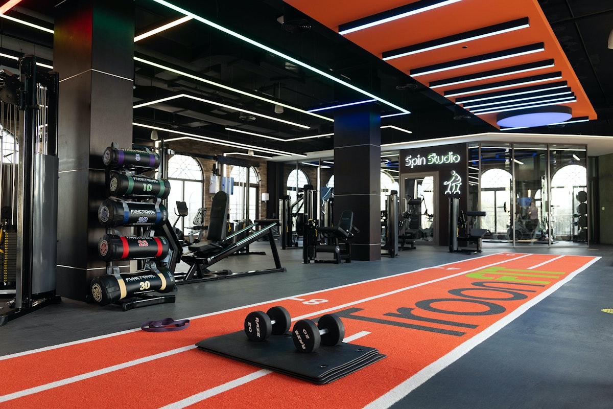 The Els Country Club Dubai Sports City A modern gym interior featuring weightlifting equipment, dumbbells, and a running track