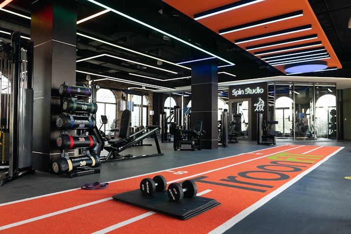A modern gym interior featuring weightlifting equipment, dumbbells, and a running track