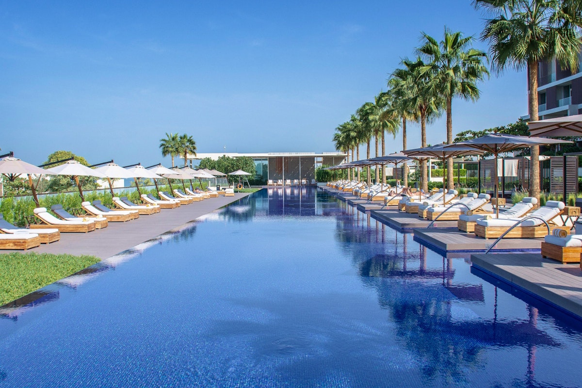 A luxurious pool lined with sun loungers and palm trees, under a clear blue sky, offering a tranquil and inviting atmosphere.