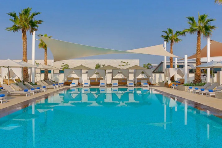 Outdoor pool with cabanas, shaded seating, and palm trees