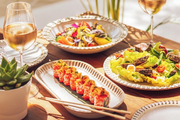 A beautifully arranged table featuring sushi, a fresh salad, and a glass of rosé wine.