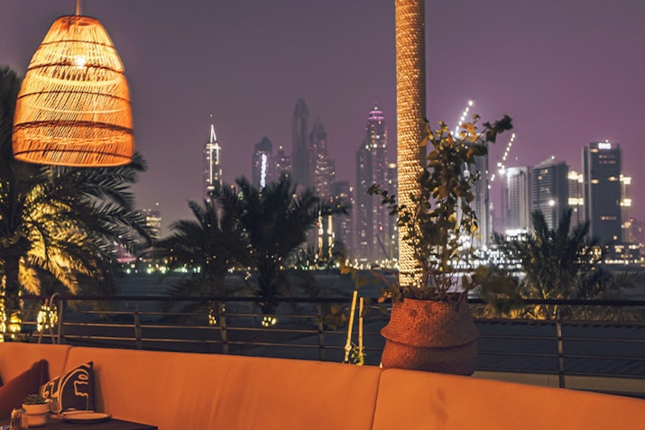 Evening view from a rooftop lounge featuring decorative lighting and a city skyline in the background.