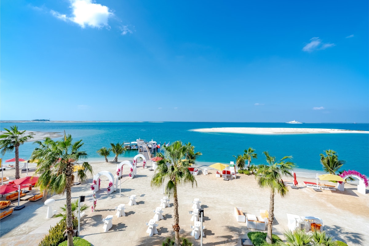 voco Monaco Beach Tropical beach with palm trees, lounge areas, and turquoise water.