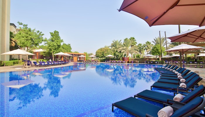 VOGO Abu Dhabi Golf Resort & Spa Large pool with blue loungers, umbrellas, and surrounding greenery.