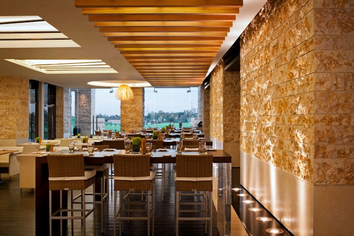 Fairways at VOGO Abu Dhabi Golf Resort & Spa Stylish restaurant interior with stone walls, wooden ceiling, and high seating.