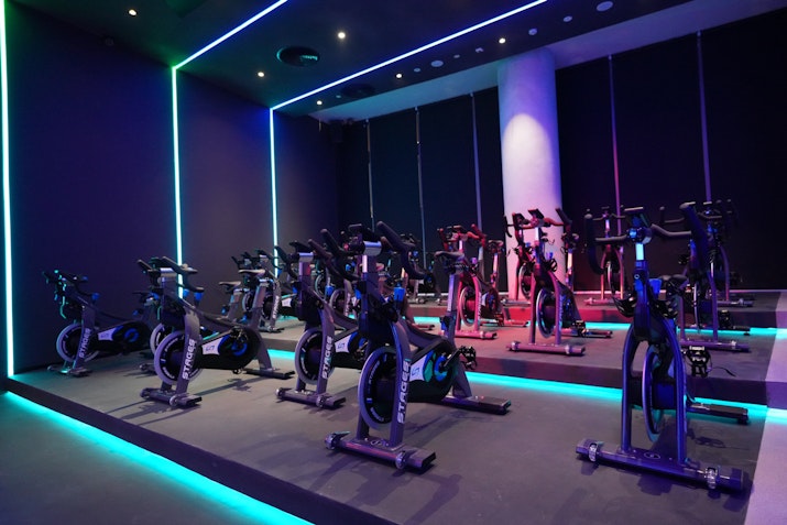 Spin studio featuring three rows of stationary bikes, colourful lights, and dark walls