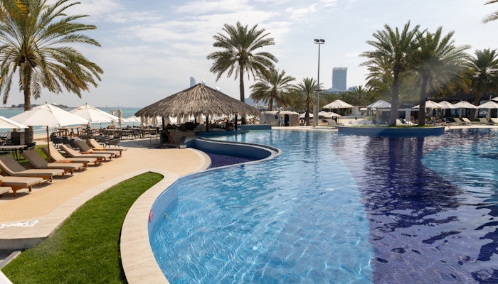 West Bay, Abu Dhabi Poolside with palm trees, cabana, and beach view.