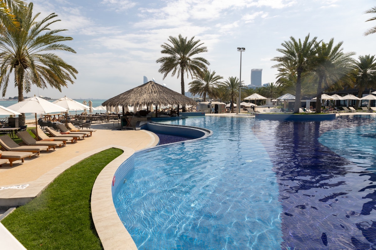 West Bay, Abu Dhabi Poolside with palm trees, cabana, and beach view.
