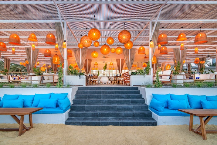West Bay Lounge Beachfront lounge area with blue seating, warm lighting, and decorative hanging lamps.