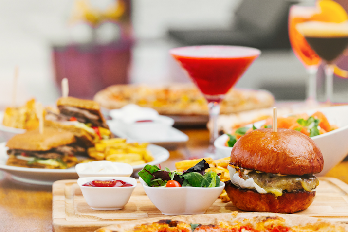 A delicious spread of food featuring a burger, fries, salad, and drinks including a cocktail and a smoothie.