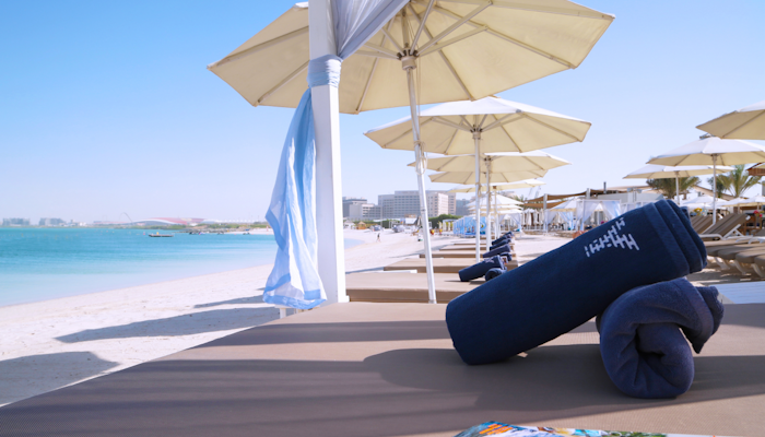 Yas Beach, Abu Dhabi Beach loungers with rolled towels under sun umbrellas, overlooking a serene beach and ocean.