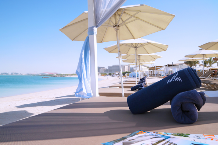 Beach loungers with rolled towels under sun umbrellas, overlooking a serene beach and ocean.
