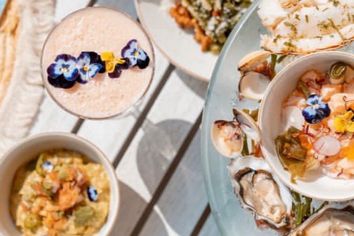 A selection of colorful seafood dishes and a cocktail with edible flowers.