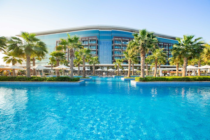 Resort pool with palm trees and modern building in the background.