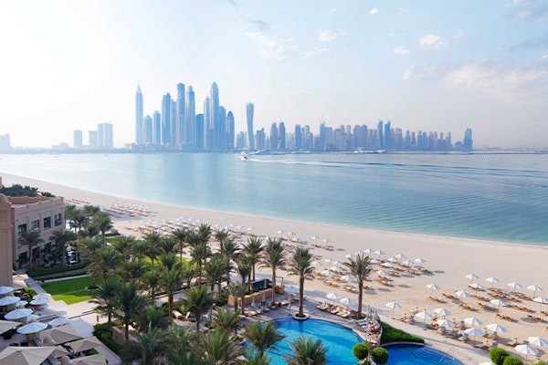 View of a beach, pool area, and a city skyline in the background.