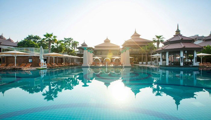 Anantara The Palm Pool with overwater bungalows in the background and sunlight reflecting on the water.