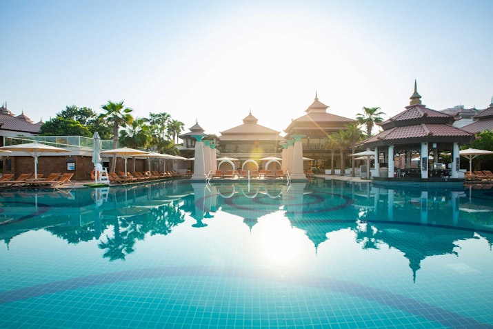 Pool with overwater bungalows in the background and sunlight reflecting on the water.