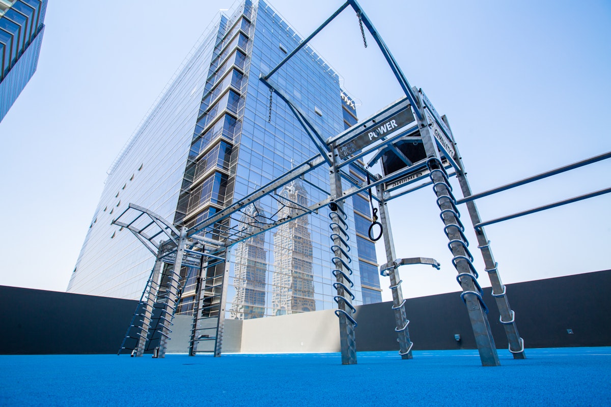 Outdoor fitness equipment setup with climbing structures and ropes, located on a rooftop with a modern building in the background.