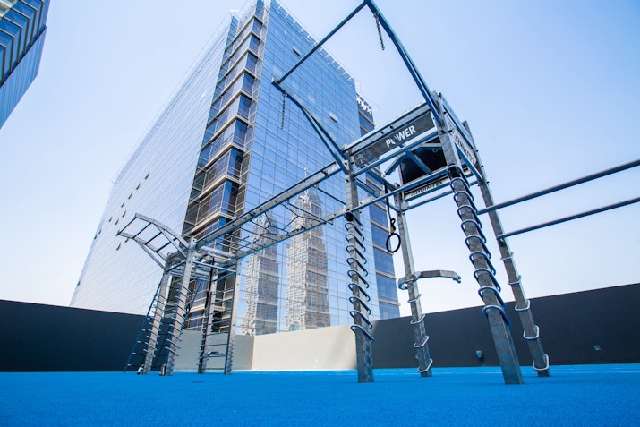 Outdoor fitness equipment setup with climbing structures and ropes, located on a rooftop with a modern building in the background.