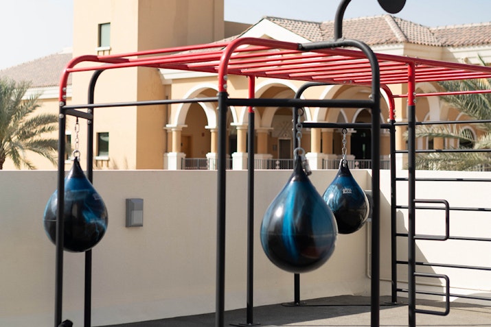 Outdoor punching bags suspended on a frame with a building in the background.