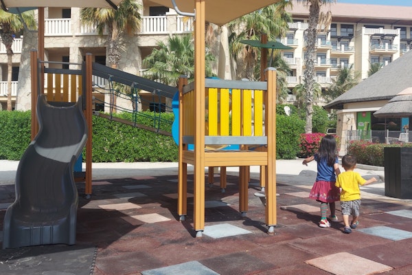 Two children walking hand-in-hand near a colorful playground with a slide and climbing structure